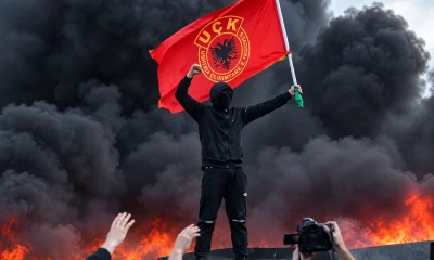 Tiranában egy maszkos tüntető a lángoló szeméttárolók fölött a Koszovói Felszabadítási Hadsereg zászlaját lengette. Egyelőre nem világos, hogy ez provokáció az Edi Rama elleni tüntetésen, vagy az albán fővárosban valóban feltűntek az UÇK támogatói, hogy a mostani tiranai zavargások farvizén a Nagy-Albánia iránti igényt népszerűsítsék